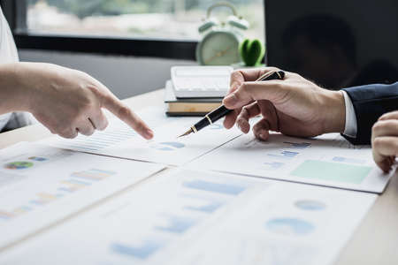 Two businessmen pointing at a chart on the document, they are startup friends together, business partners shaking hands after brainstorming and planning a startup company. Startup company concept.の写真素材