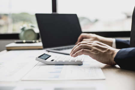 Man pressing white calculator, business man sitting in a private office at his company, he runs a startup company, he's a young man starting a business. Management concept of startup company.の写真素材