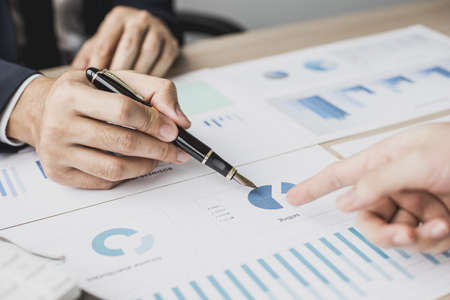 Two businessmen pointing at a chart on the document, they are startup friends together, business partners shaking hands after brainstorming and planning a startup company. Startup company concept.の写真素材
