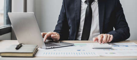 Man using laptop and pressing calculator, business man sitting in private office at his company, he runs a startup company, he's a young man starting a business. Management concept of startup company.の写真素材