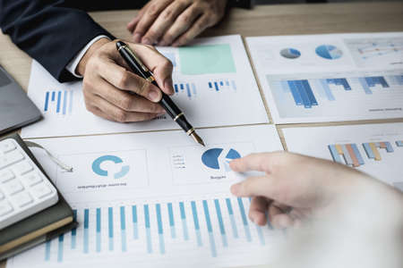 Two businessmen pointing at a chart on the document, they are startup friends together, business partners shaking hands after brainstorming and planning a startup company. Startup company concept.の写真素材