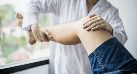 A professional physiotherapist is stretching the patient's legs, the patient has muscle dysfunction due to hard work, most often an office worker who has problems sitting for long periods of time.の写真素材