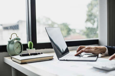 Man using laptop and pressing calculator, business man sitting in private office at his company, he runs a startup company, he's a young man starting a business. Management concept of startup company.の写真素材
