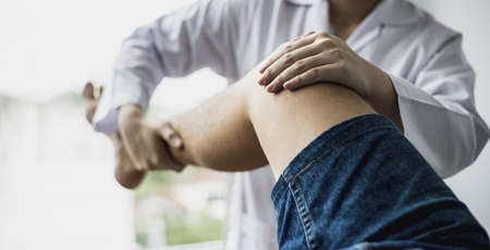 A professional physiotherapist is stretching the patient's legs, the patient has muscle dysfunction due to hard work, most often an office worker who has problems sitting for long periods of time.の写真素材
