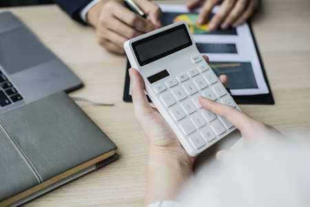 The head of the finance department presents the financial information to the executive, she is pressing the white calculator to calculate the validation number. Concept of financial management.の写真素材