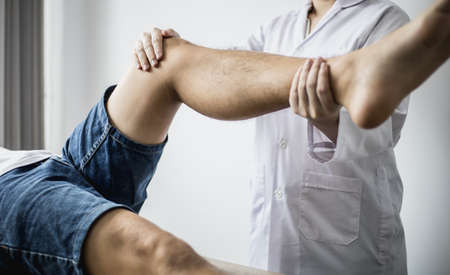 A professional physiotherapist is stretching the patient's legs, the patient has muscle dysfunction due to hard work, most often an office worker who has problems sitting for long periods of time.の写真素材