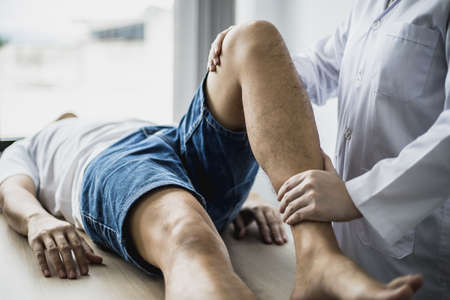A professional physiotherapist is stretching the patient's legs, the patient has muscle dysfunction due to hard work, most often an office worker who has problems sitting for long periods of time.の写真素材