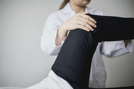 A professional physiotherapist is stretching the patient's legs, the patient has muscle dysfunction due to hard work, most often an office worker who has problems sitting for long periods of time.の写真素材