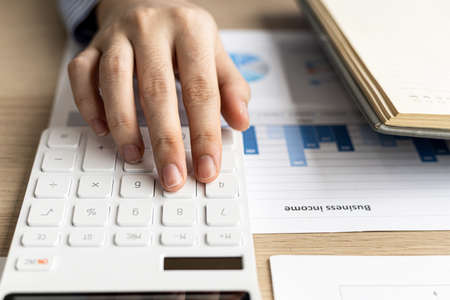 Female auditor pressing white calculator, she is a private company auditor, she is reviewing numbers of company financial statements before presenting them to senior management. Audit concept.の写真素材