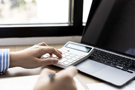 Female auditor pressing white calculator, she is a private company auditor, she is reviewing numbers of company financial statements before presenting them to senior management. Audit concept.の写真素材