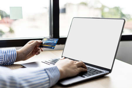 Woman typing on a laptop keyboard and holding a credit card, she fills in her credit card information on a laptop shopping app to pay for the order. Online shopping concept using credit card payments.の写真素材