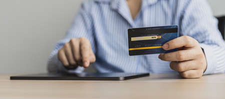 A woman typing on a tablet and holding a credit card, she fills in her credit card information on a shopping app on her laptop to pay for the order. Online shopping concept using credit card payments.の写真素材