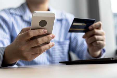 A woman holding a cell phone and credit card, she fills in her credit card information in a mobile...