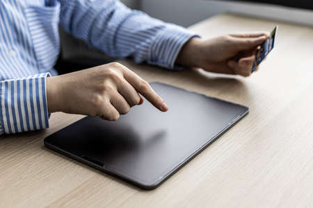 A woman typing on a tablet and holding a credit card, she fills in her credit card information on a...