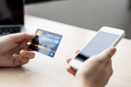 A woman holding a cell phone and credit card, she fills in her credit card information in a mobile...