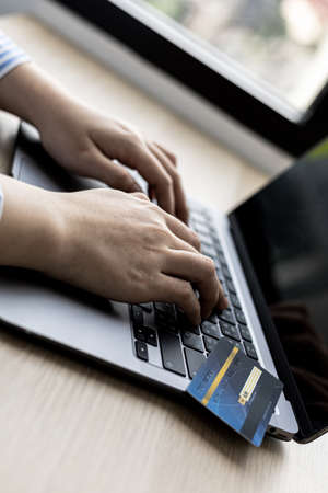 Woman typing on a laptop keyboard and holding a credit card, she fills in her credit card information on a laptop shopping app to pay for the order. Online shopping concept using credit card payments.の写真素材