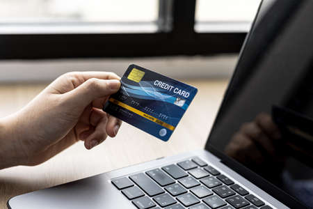 Woman typing on a laptop keyboard and holding a credit card, she fills in her credit card...