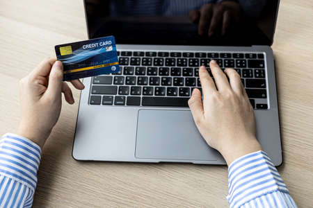 Woman typing on a laptop keyboard and holding a credit card, she fills in her credit card information on a laptop shopping app to pay for the order. Online shopping concept using credit card payments.の写真素材