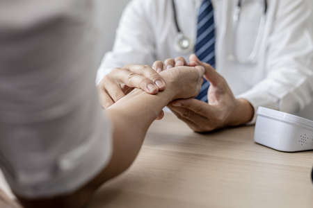 Close-up photo Doctor holding pulse on patient's wrist in the examination room, patient visits doctor due to discomfort. The concept of visiting a doctor when sick for a diagnosis.の写真素材