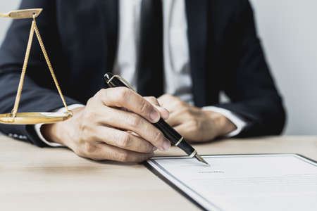 A male lawyer is signing a plea agreement with a client in a fraud case, in which the client has filed a lawsuit against an employee at a company that commits the fraud. Fraud litigation concept.の写真素材