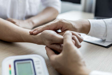 Close-up photo Doctor holding pulse on patient's wrist in the examination room, patient visits doctor due to discomfort. The concept of visiting a doctor when sick for a diagnosis.の写真素材