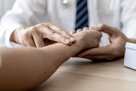 Close-up photo Doctor holding pulse on patient's wrist in the examination room, patient visits doctor due to discomfort. The concept of visiting a doctor when sick for a diagnosis.の写真素材