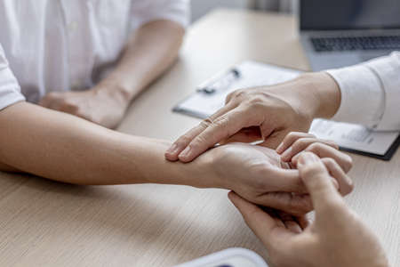 Close-up photo Doctor holding pulse on patient's wrist in the examination room, patient visits doctor due to discomfort. The concept of visiting a doctor when sick for a diagnosis.の写真素材