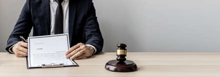 A male lawyer is signing a plea agreement with a client in a fraud case, in which the client has filed a lawsuit against an employee at a company that commits the fraud. Fraud litigation concept.の写真素材