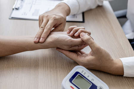 Close-up photo Doctor holding pulse on patient's wrist in the examination room, patient visits doctor due to discomfort. The concept of visiting a doctor when sick for a diagnosis.の写真素材