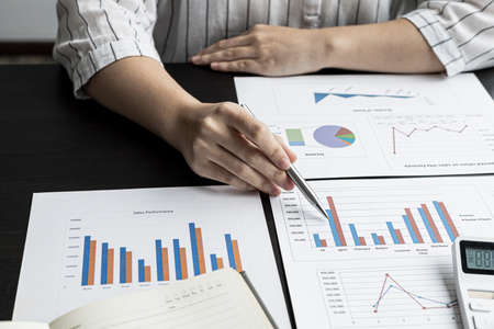 Close-up businesswoman holding a pen pointing to a bar graph document of company financial data, she is reviewing the company's monthly financial documents. Finance concepts and money management.の写真素材