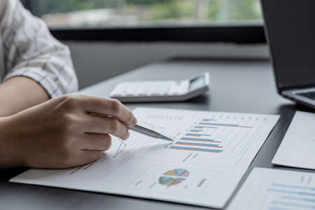 Close-up businesswoman holding a pen pointing to a bar graph document of company financial data, she is reviewing the company's monthly financial documents. Finance concepts and money management.の写真素材
