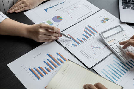 Two businessmen are reviewing the earnings summary and company financial documents that each...