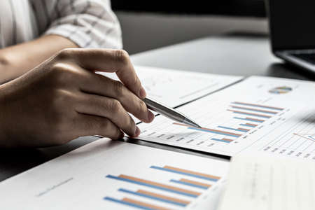 Close-up businesswoman holding a pen pointing to a bar graph document of company financial data, she is reviewing the company's monthly financial documents. Finance concepts and money management.の写真素材