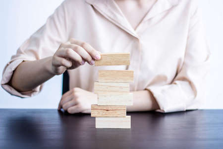 A woman playing with a wooden block, she is picking up a wooden block on top, a businesswoman building a wooden block is the idea of a businessman running a company to grow and manage risks.の写真素材