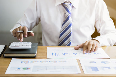 A businessman is pressing a white calculator, he is calculating numbers to check the accuracy of company financial information prepared by the finance department. Company finance concept.の写真素材