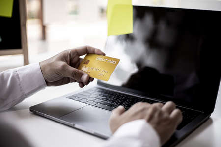 Businessman holds a yellow credit card, the businessman is filling out credit card information to...
