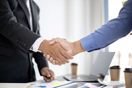 Close-up two business men holding hands, Two businessmen are agreeing on business together and shaking hands after a successful negotiation. Handshaking is a Western greeting or congratulation.の写真素材