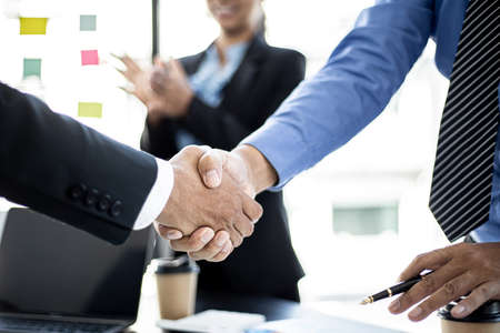 Close-up two business men holding hands, Two businessmen are agreeing on business together and shaking hands after a successful negotiation. Handshaking is a Western greeting or congratulation.の写真素材