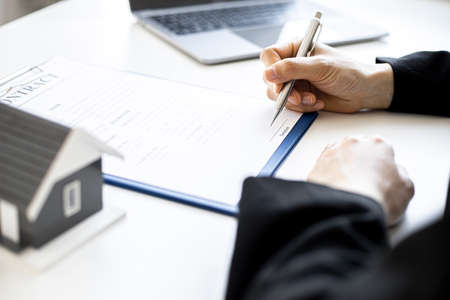 A woman's home salesperson is checking documents for a house purchase contract before letting the customer sign a contract, on the table is a gray miniature house model, real estate trading ideas.の写真素材