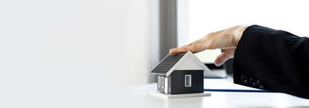 A woman's home salesman touches the gray model on the table, she is describing the house contract in detail to the client. Real estate trading ideas. Panorama banner background with copy space.の写真素材