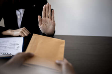 Businesswoman raised her hand to deny accepting a bribe from a business partner, a brown envelope containing a large number of dollar bills as money for bribery, a corruption concept.の写真素材