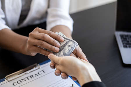 Two business women are committing corruption, a business woman in a black suit receives a dollar from a business partner which is the money used to bribe, bribery is illegal. Concept of corruption.の写真素材