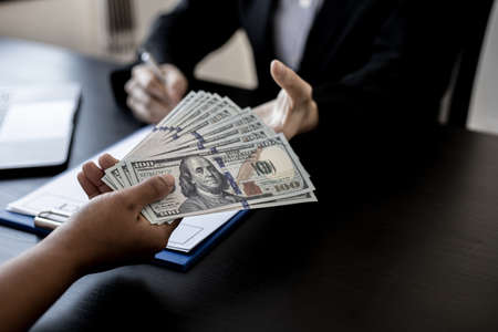 Two business women are agreeing to a contract with a corrupt company, bribing a lot of dollars in brown envelopes, and corruption is illegal. The concept of corruption.の写真素材