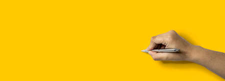Person's hand holding a pen and about to write, Isolated on a yellow background .の写真素材