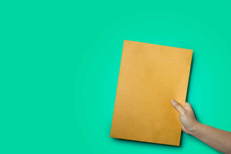 Close up of hand holding a brown envelope, A4 size paper envelope, Isolated on green backgroundの写真素材