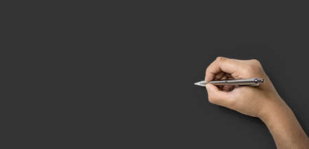 Person's hand holding a pen and about to write, Isolated on a dark gray backgroundの写真素材