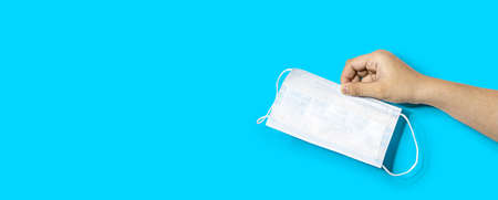 A person's hand is holding a mask, a mask used to prevent the spread of virus. Used masks should be disposed of properly and properly. Isolated on a blue backgroundの写真素材