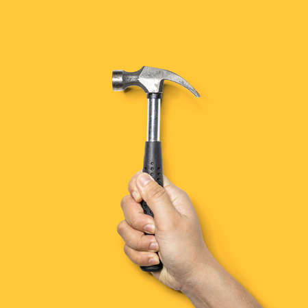 Person holding a small hammer with a black handle, hammer is a tool for hammer nails, Isolated on yellow backgroundの写真素材