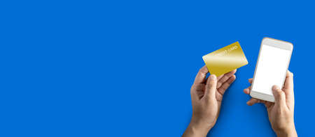 Left hand holding a golden credit card, right hand holding a white mobile phone, Isolated on blue...