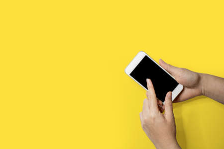Hand holding mobile phone, Left hand touching smart phone screen, Isolated on yellow backgroundの写真素材